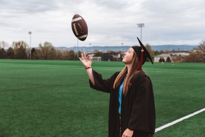 Leah Wood throwing a football in her cap and gown