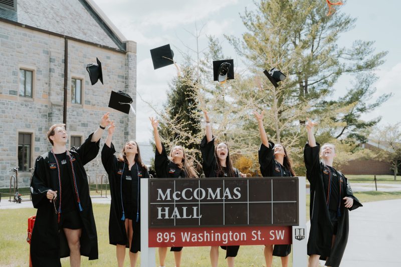 Group of students throw grad caps next to McComas Hall's building sign